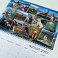 A spiral-bound August 2027 desk calendar page featuring a collage of dog photographs across the top and a weekly calendar grid on a white background.
