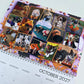 A spiral-bound October 2027 desk calendar page featuring a collage of pet photos dressed in Halloween costumes, with pumpkin decorations and the date October 2027 visible at the bottom.