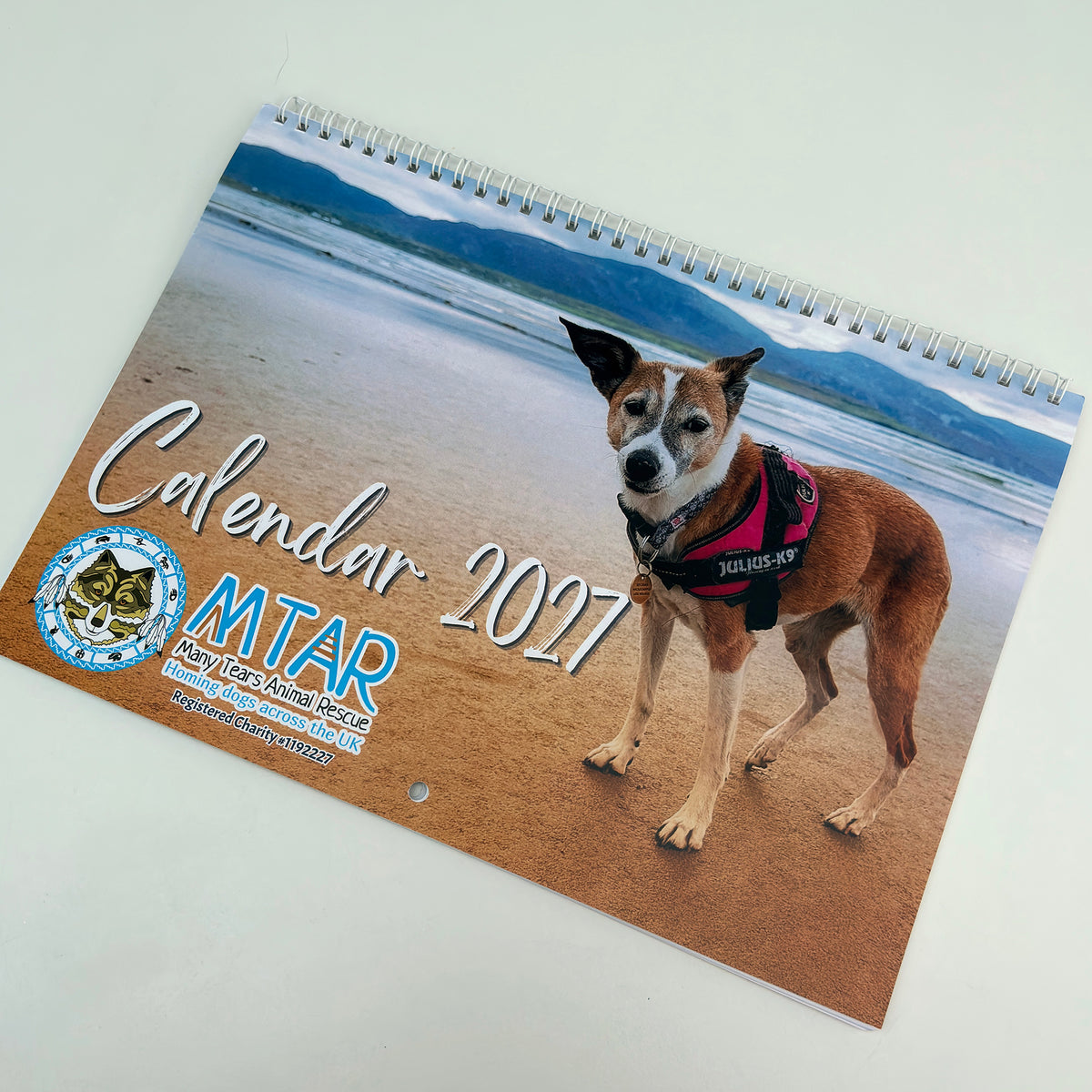 A 2027 spiral bound Many Tears Animal Rescue calendar. The calendar cover shows a dog on a beach.