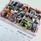 A spiral-bound 2027 desk calendar page featuring a collage of various dog photos, pink floral borders, and the text 'I love you' with a heart. The calendar is photographed on a clean white surface.