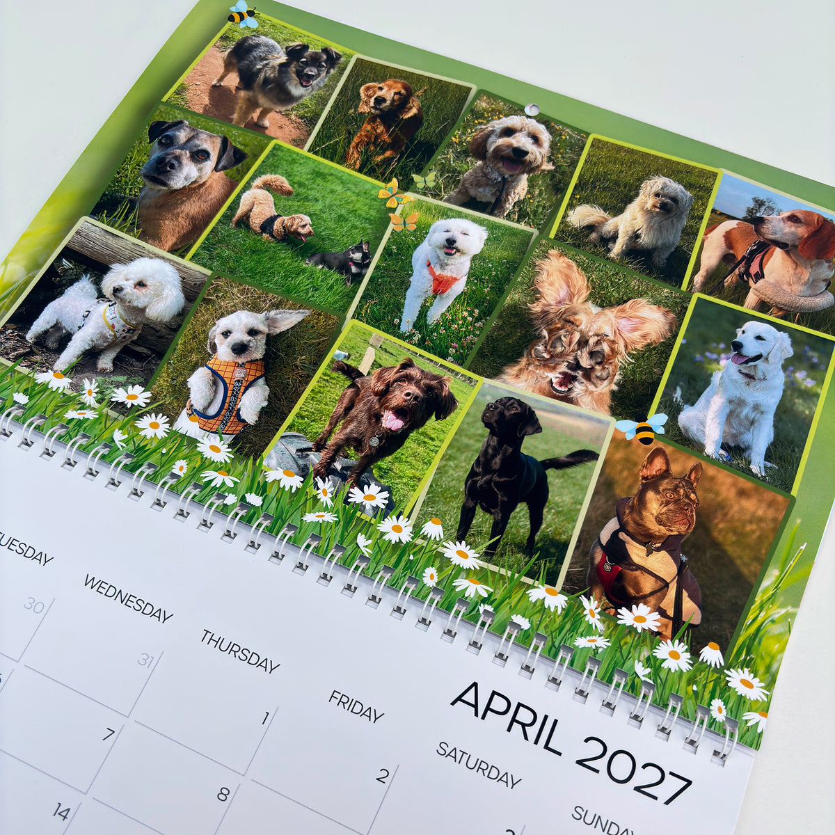 A spiral-bound monthly calendar page for April 2027, featuring a grid of 16 dog photos.